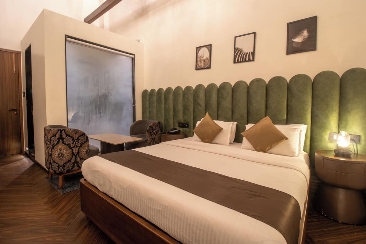 A hotel room with a large bed, a desk, a chair, a wardrobe, and a mirror on the wall.