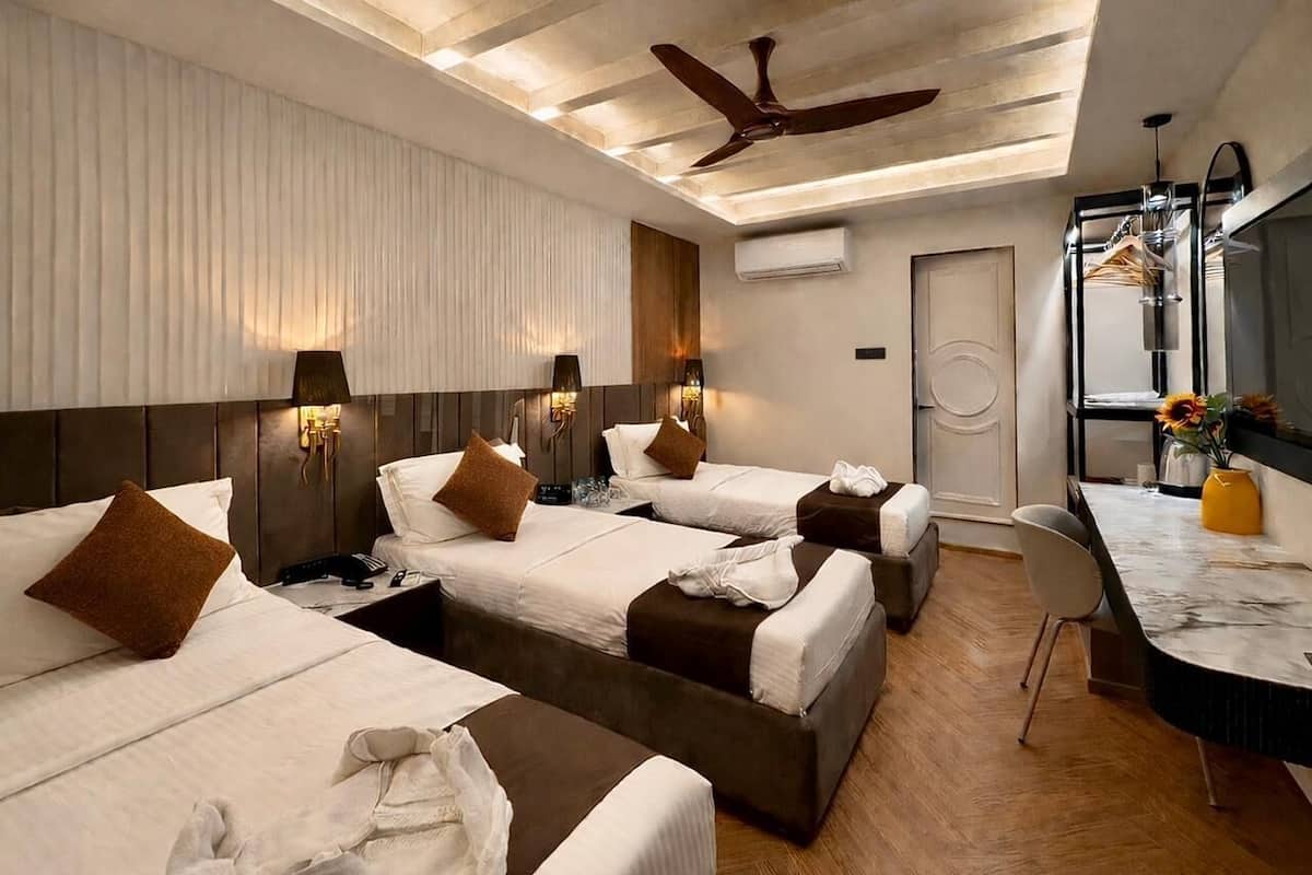 A hotel room with three beds, a desk, a chair, a ceiling fan, and a wall-mounted air conditioner.
