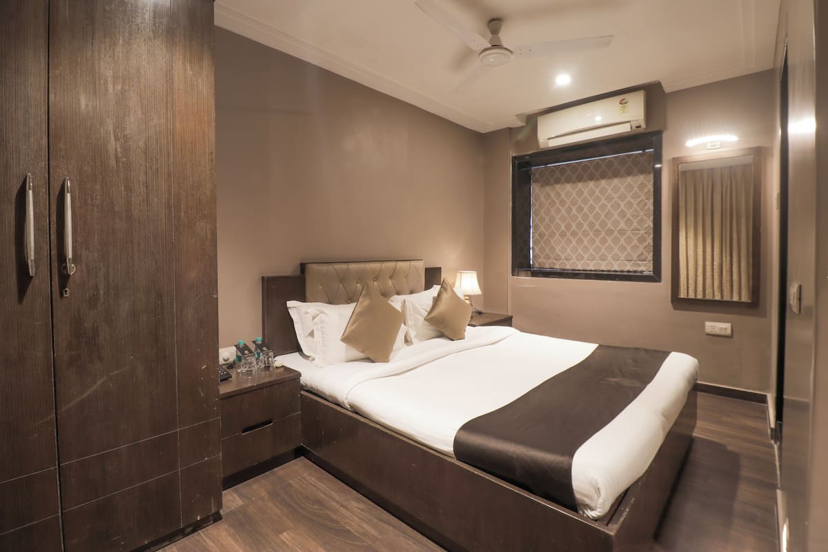 A hotel room with a large bed, a wardrobe, a bedside table, a nightstand, a window with curtains, and a ceiling fan.