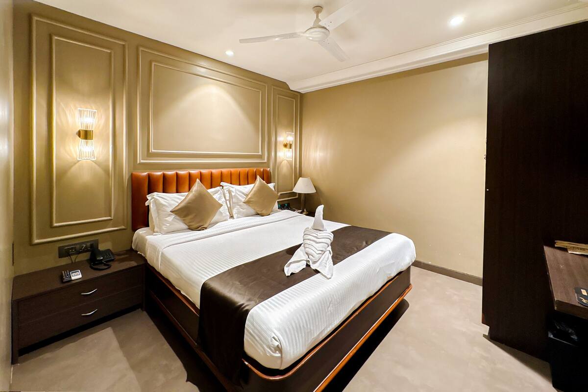 A hotel room with a large bed, a ceiling fan, bedside lamps, and a nightstand with a phone and charger.