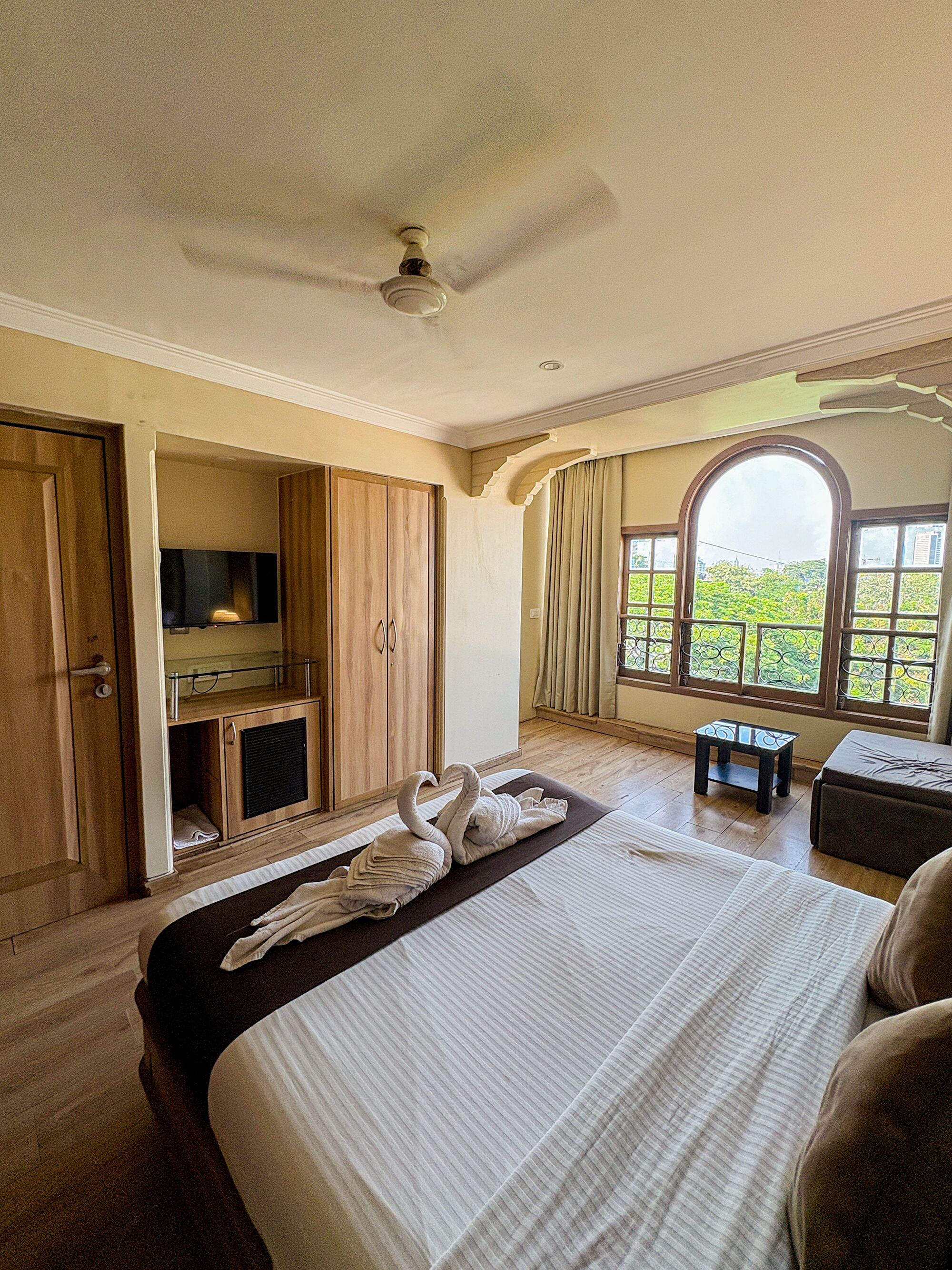 A bedroom with a bed, a TV, a wardrobe, and a window with a view.