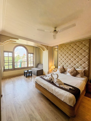 Amplia habitación con una cama grande, zona de estar y vistas a un paisaje urbano a través de ventanales arqueados.