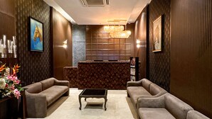 A lobby with a reception desk, sofas, a coffee table, and decorative elements like framed artwork and a chandelier. - Gulf Hotel Colaba (Mumbai)