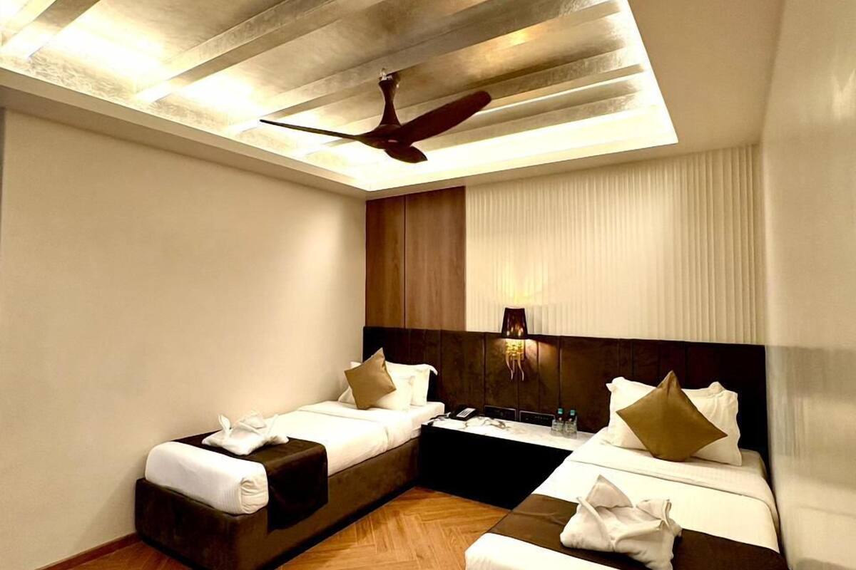 A hotel room with a sloped ceiling, two beds, a wooden floor, a ceiling fan, and a nightstand with a lamp.