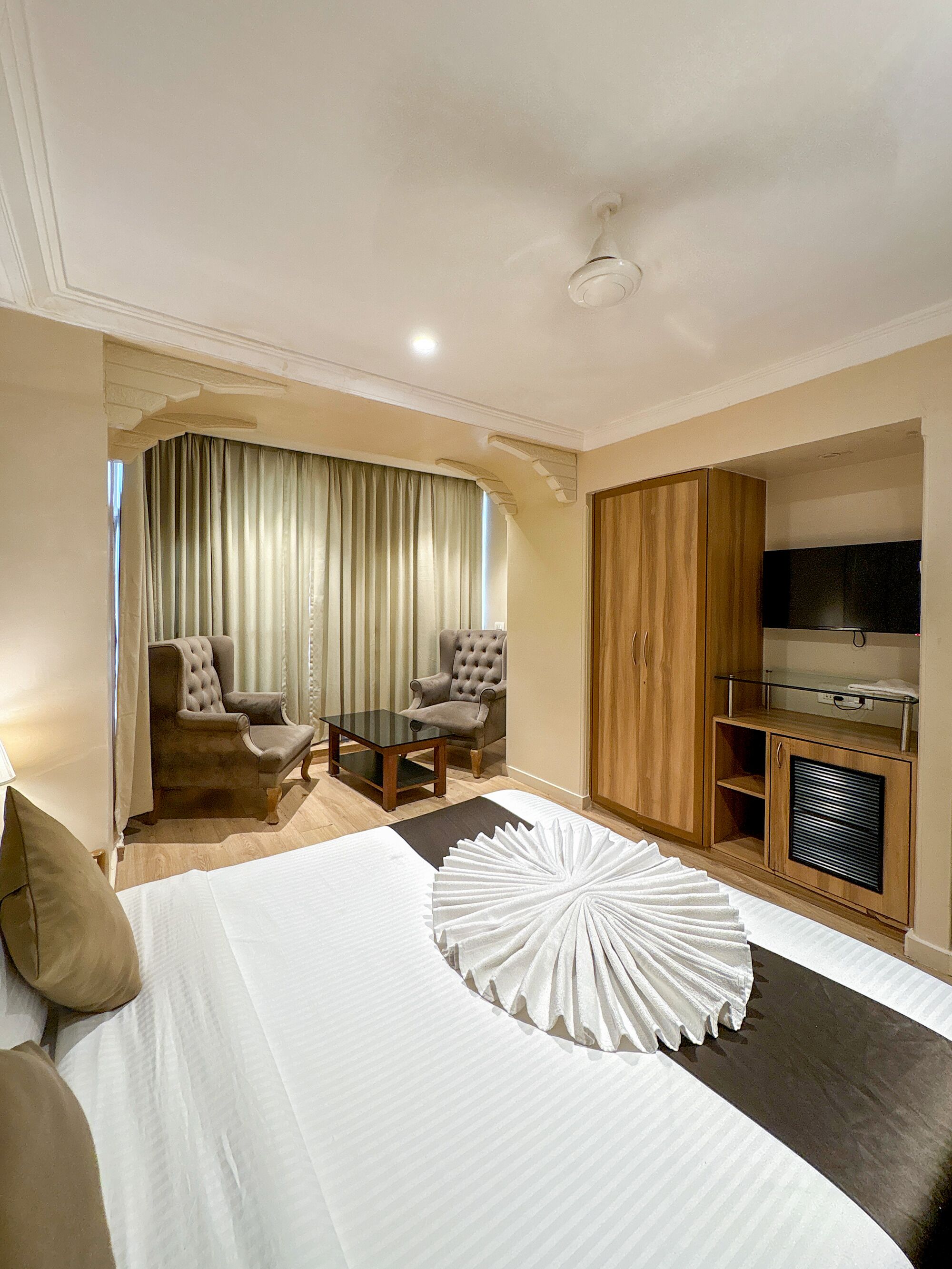 A hotel room with a bed, two armchairs, a small table, a TV, and a wardrobe.