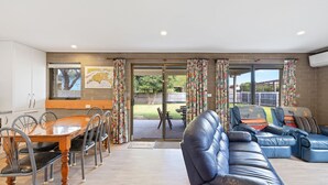 Ampla sala de estar com mesa de jantar, cadeiras, sofá e vista para o quintal através de grandes portas de vidro deslizantes.