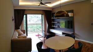 Un salon moderne comprenant un canapé, une table à manger, des chaises, un ventilateur de plafond, un téléviseur fixé au mur et une grande fenêtre avec des rideaux.