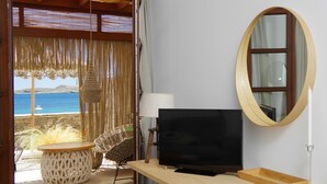 A room with a wooden desk, a television, a round mirror, and a wicker chair. - Syros Wellness Luxury Suites (Syros)
