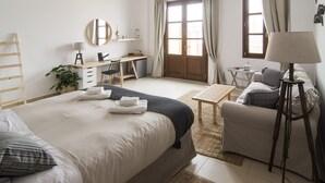 A well-lit bedroom with a bed, bedside table, chair, desk, and a small table with a lamp. - Syros Wellness Luxury Suites (Syros)