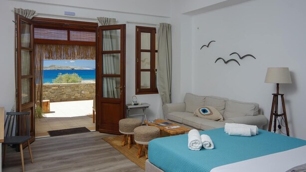 A hotel room with a bed, a sofa, a small table, and a view of the sea. - Syros Wellness Luxury Suites (Syros)
