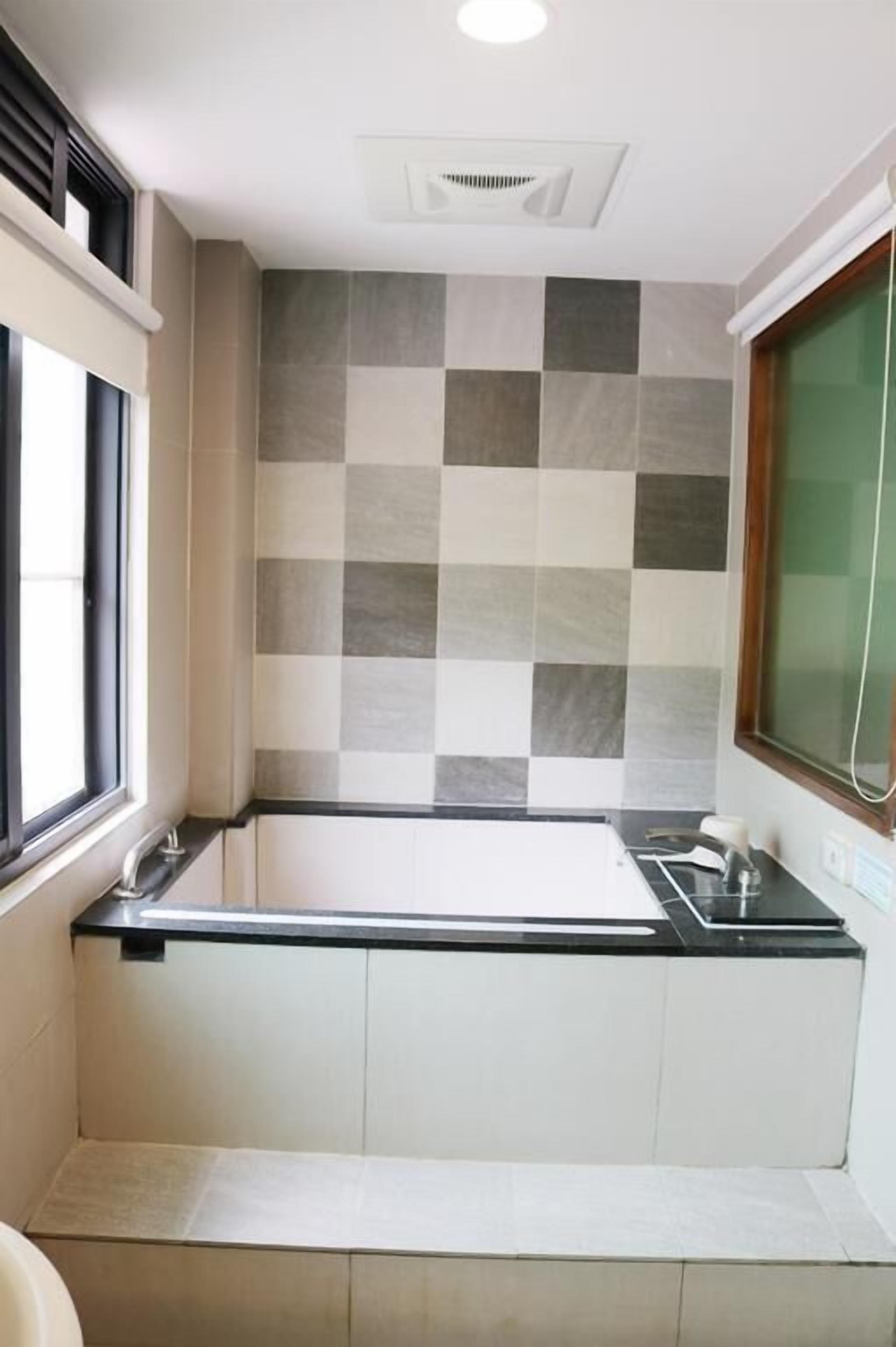 A bathroom with a checkered tile backsplash, a black countertop, and a white sink.