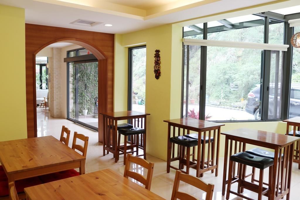 Um restaurante com mesas e cadeiras de madeira, grandes janelas com vista para o exterior e uma parede amarela.