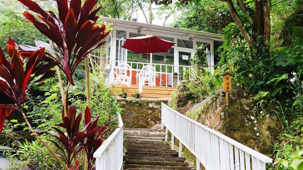 Una escalera conduce a una zona de estar al aire libre cubierta, con sillas blancas y un paraguas rojo.