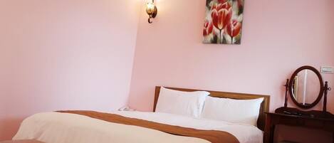A neatly made bed with white and brown linens, a bedside table with a mirror, and a wall-mounted light fixture.