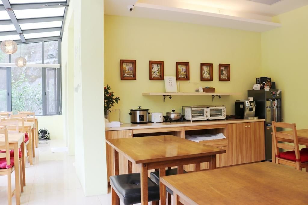 Una cocina con armarios de madera, una encimera con una cafetera, un microondas y una estufa. Hay cuadros en la pared y una ventana con vistas a zonas verdes.