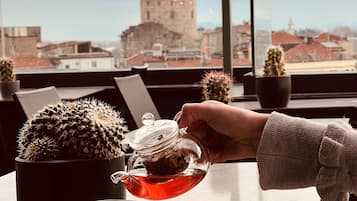 Iemand giet thee uit een glazen theepot in een kopje, met een cactusplant in een pot op de tafel.