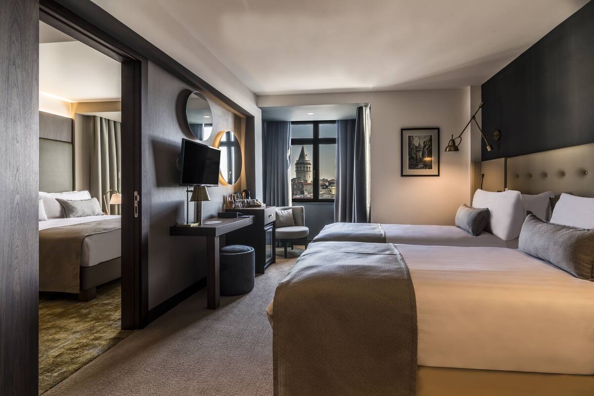 A hotel room with two beds, a desk, a chair, a TV, and a view of a historic tower.
