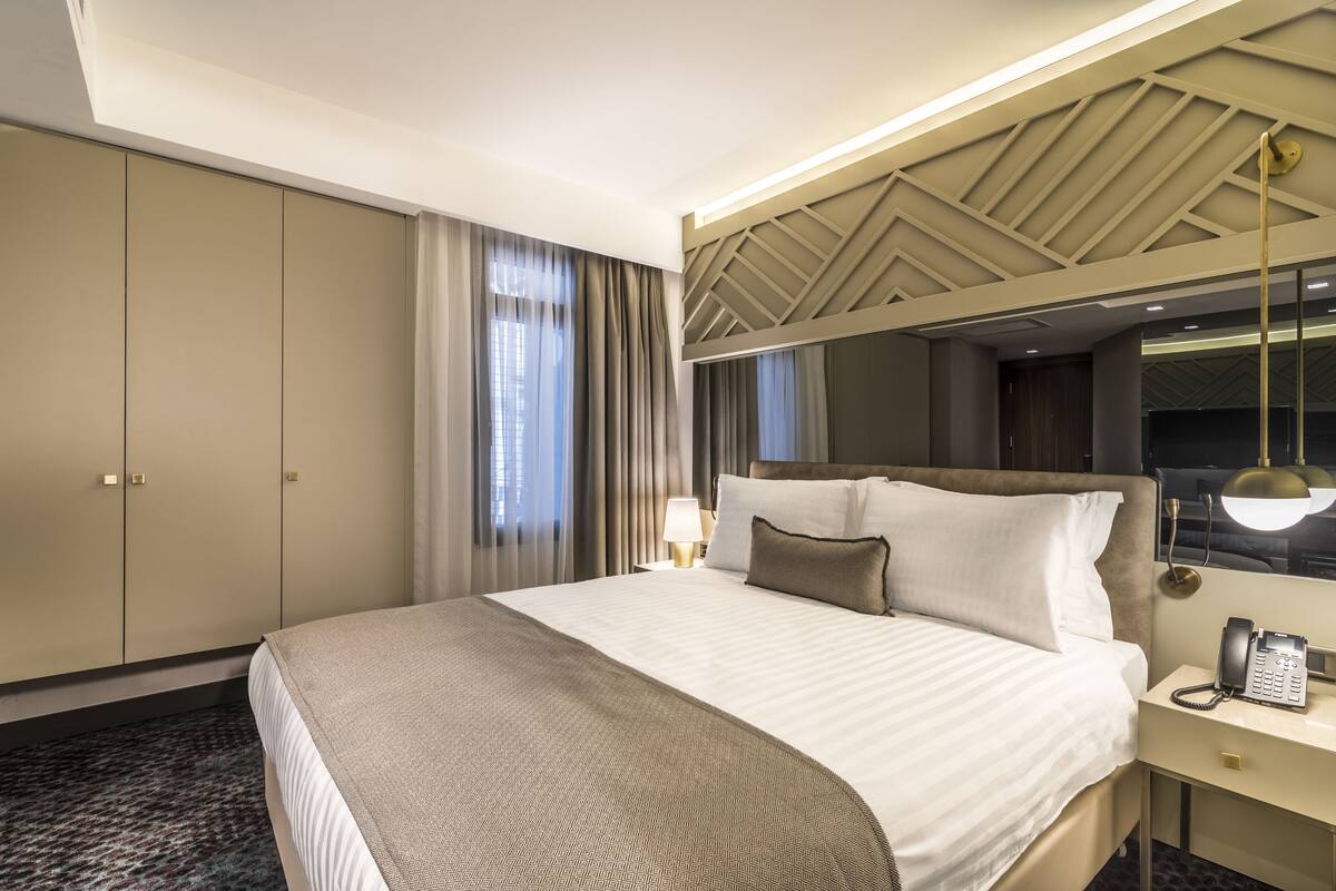 A hotel room with a large bed, a bedside telephone, a desk with a lamp, and a wardrobe.