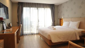 A hotel room with a bed, a desk, a chair, a coffee maker, and a view of the outside through large windows. - Imperial Saigon Hotel (Ho Chi Minh City)