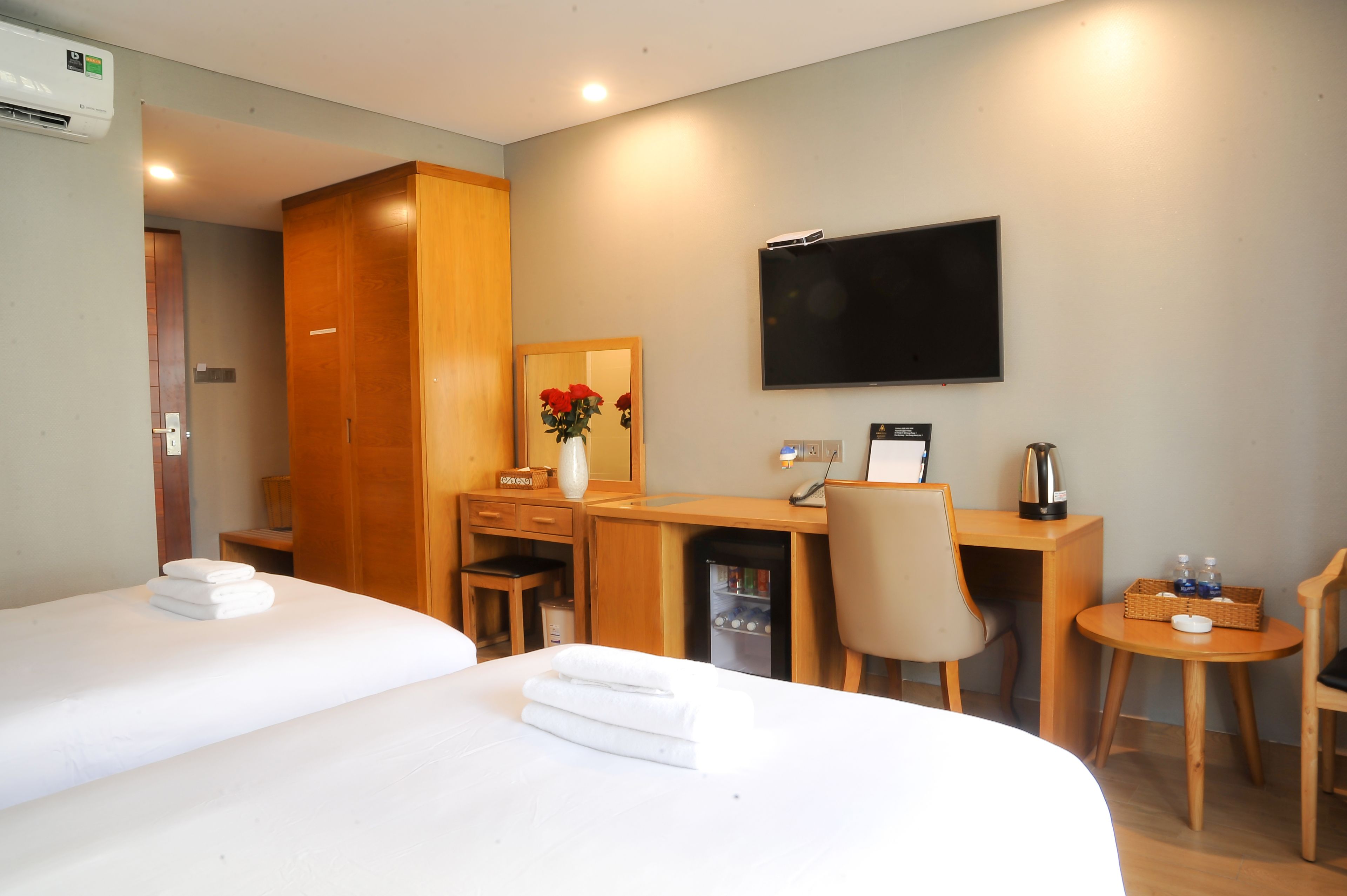 Habitación de hotel con dos camas, un escritorio con silla, televisor y una mesita con cesta.