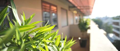 A balcony with potted plants, a red awning, and a building in the background.