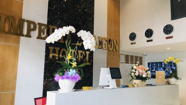 A hotel reception desk with a large sign reading "IMPERIAL HOTEL," a computer monitor, a Samsung Pay card reader, and a floral arrangement. - Imperial Saigon Hotel (Ho Chi Minh City)