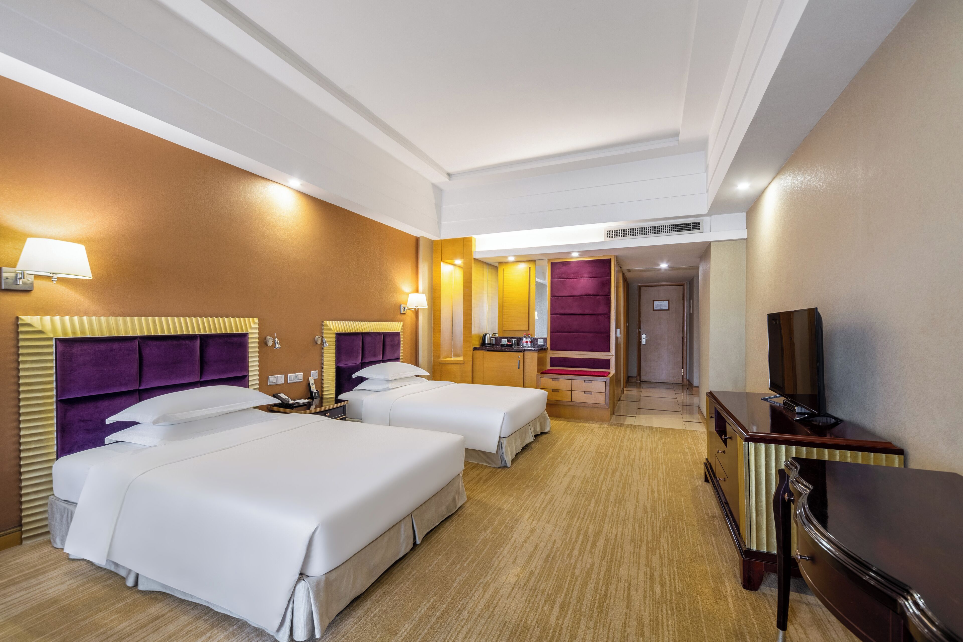 A hotel room with two beds, a desk, a TV, and a bathroom visible through an open door.