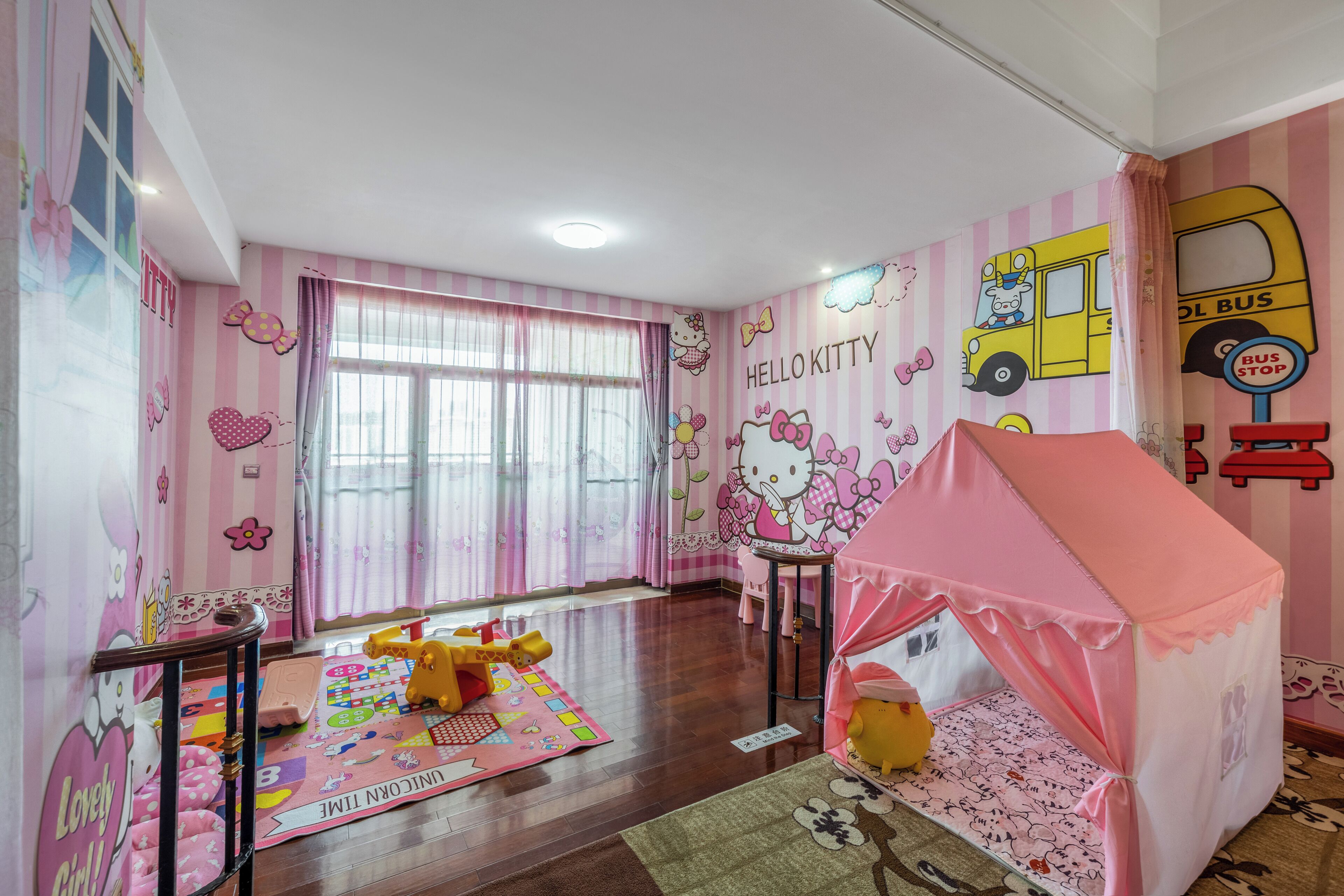 A children's room with pink and white striped walls, a Hello Kitty mural, a pink tent, and a play mat.