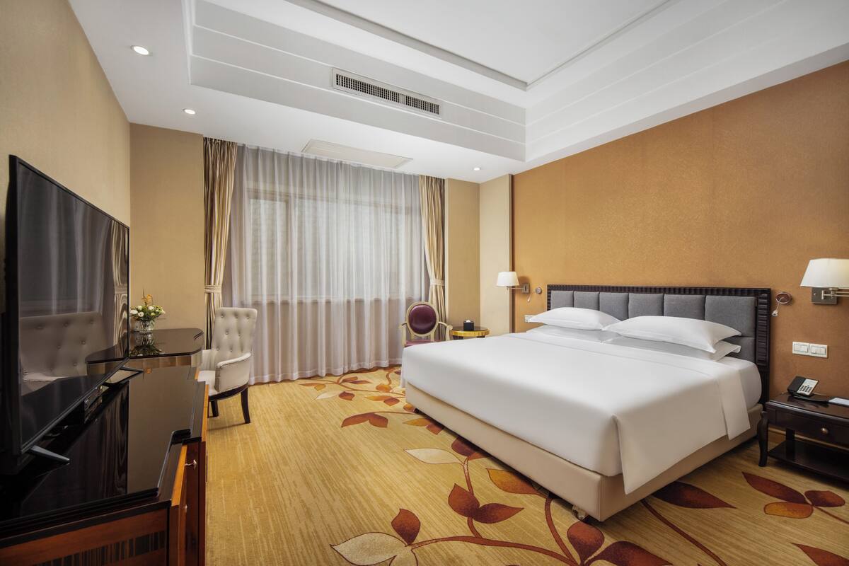 Habitación de hotel con una cama grande, un televisor de pantalla plana, un escritorio con una silla y una ventana con cortinas.