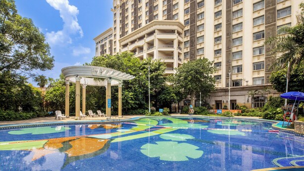 A swimming pool with a gazebo and lounge chairs, surrounded by lush greenery and a tall building in the background. - Xinhui Country Garden Phoenix Hotel (Jiangmen)