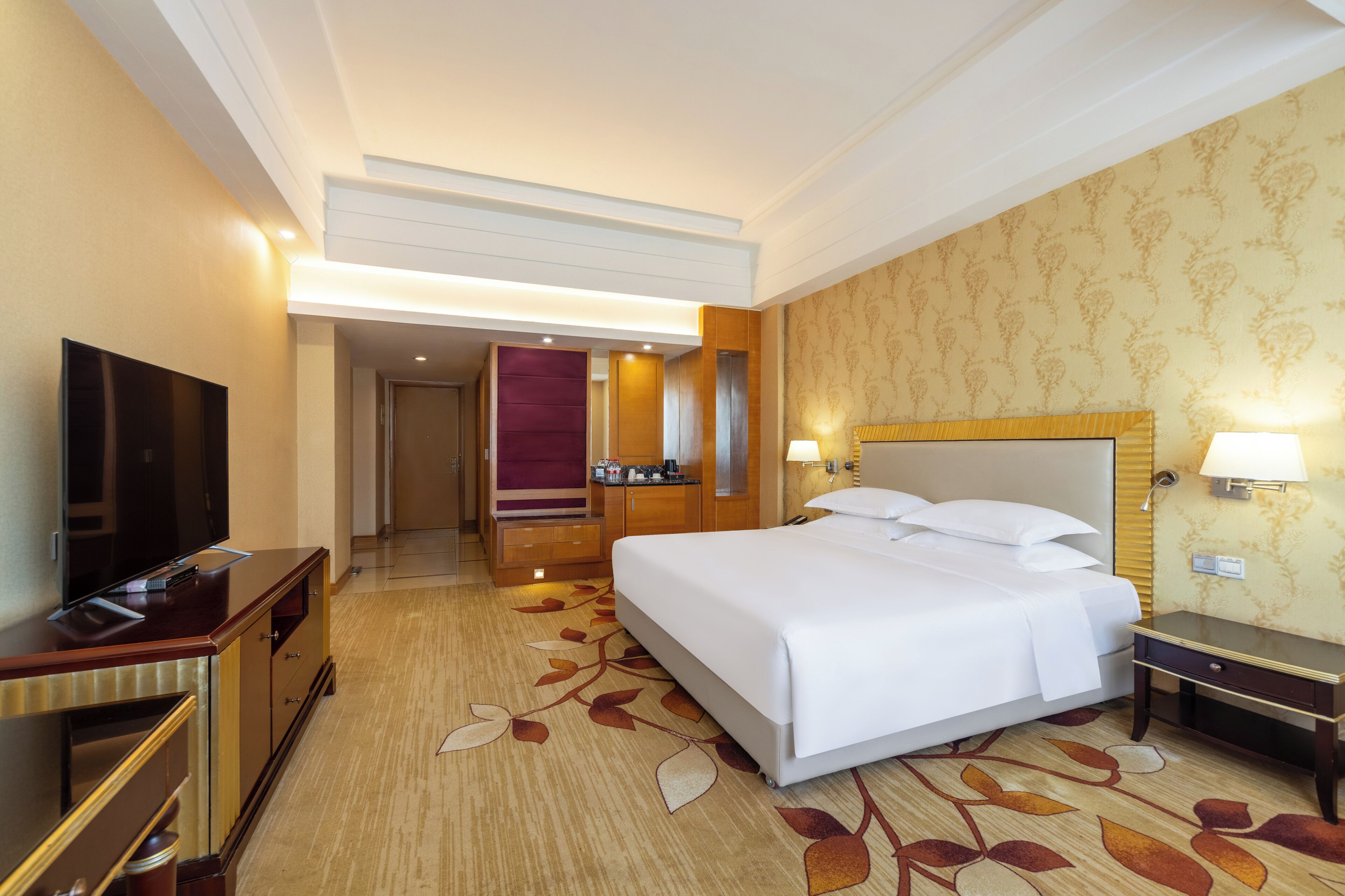 Une chambre d’hôtel dotée d’un grand lit, d’un téléviseur à écran plat, d’un bureau avec une lampe et d’une salle de bain visible à travers une porte ouverte.
