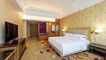 Habitación de hotel con una cama grande, televisión de pantalla plana, escritorio con lámpara y baño visible a través de una puerta abierta.
