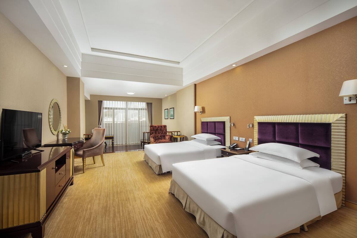 Habitación de hotel con dos camas, un escritorio, una silla, un televisor y una ventana con cortinas.