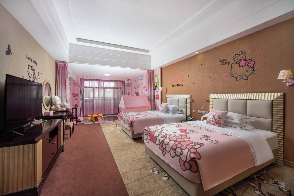 Habitación de hotel con dos camas, televisión, escritorio y ventana grande con cortinas rosadas.