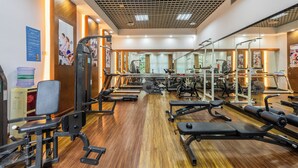 Une salle de sport équipée de divers appareils d’exercice, dotée d’un plancher en bois et de miroirs sur les murs.