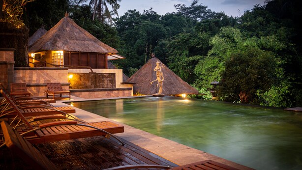 A poolside area with thatched-roof structures, lounge chairs, and a statue. - The Pari Sudha (Ubud)