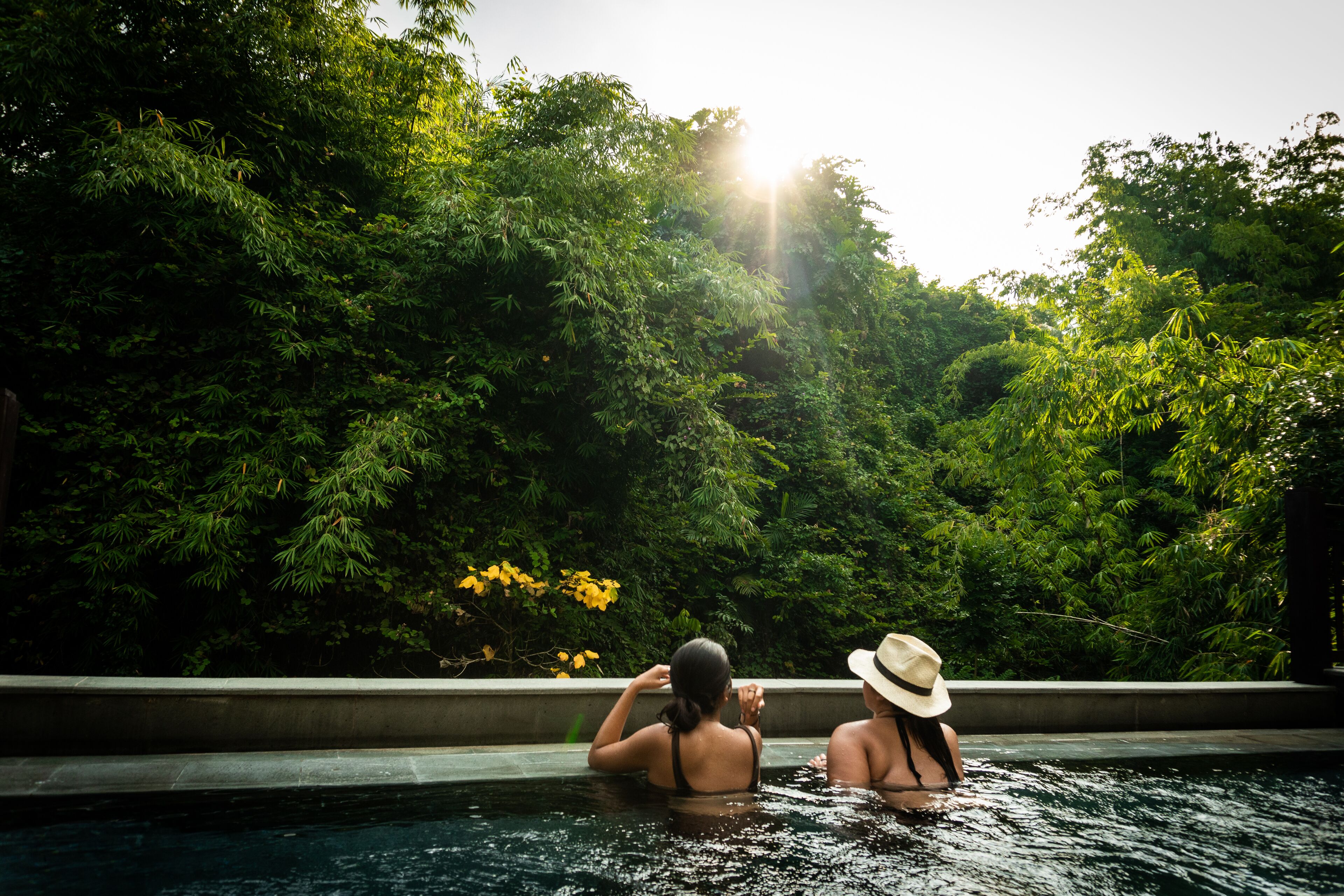 Two people in a swimming pool surrounded by lush greenery.