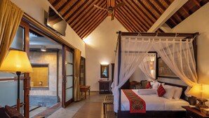 A bedroom with a four-poster bed, a sitting area with a chair, a desk, and a television. - The Pari Sudha (Ubud)