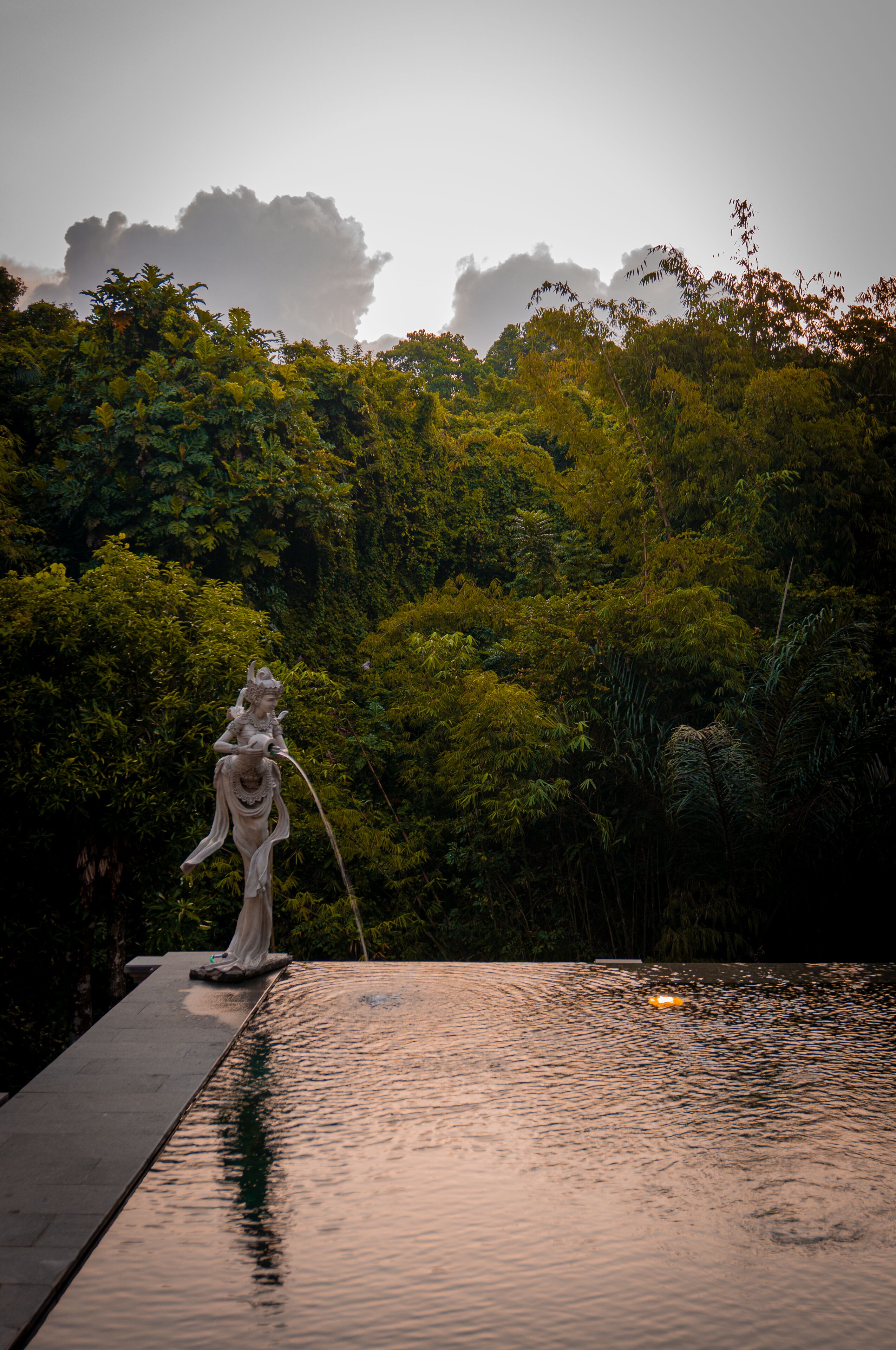 Una estatua en una fuente de agua con un bosque de fondo.