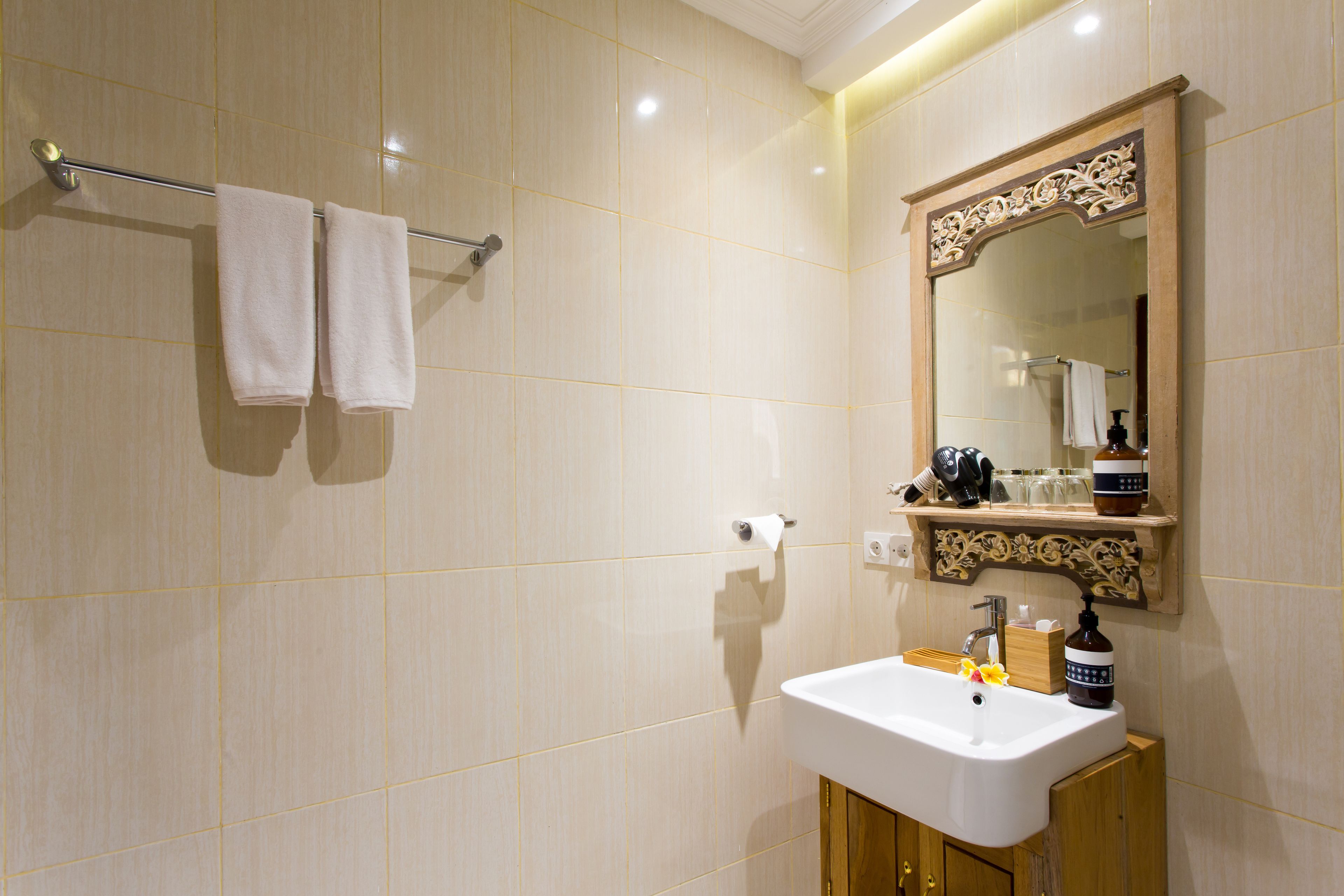 Une salle de bain avec un lavabo blanc, un miroir doté d’un cadre orné et deux serviettes suspendues à un porte-serviettes.