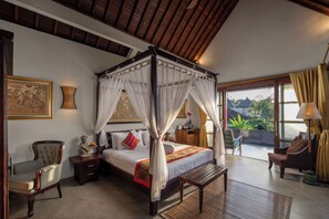 A four-poster bed with a canopy, a wooden bench, a chair, and a nightstand with a lamp. - The Pari Sudha (Ubud)