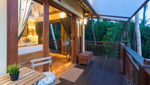 A wooden deck with a bench and a small table, a covered area with a view of greenery, and a wooden railing. - The Pari Sudha (Ubud)