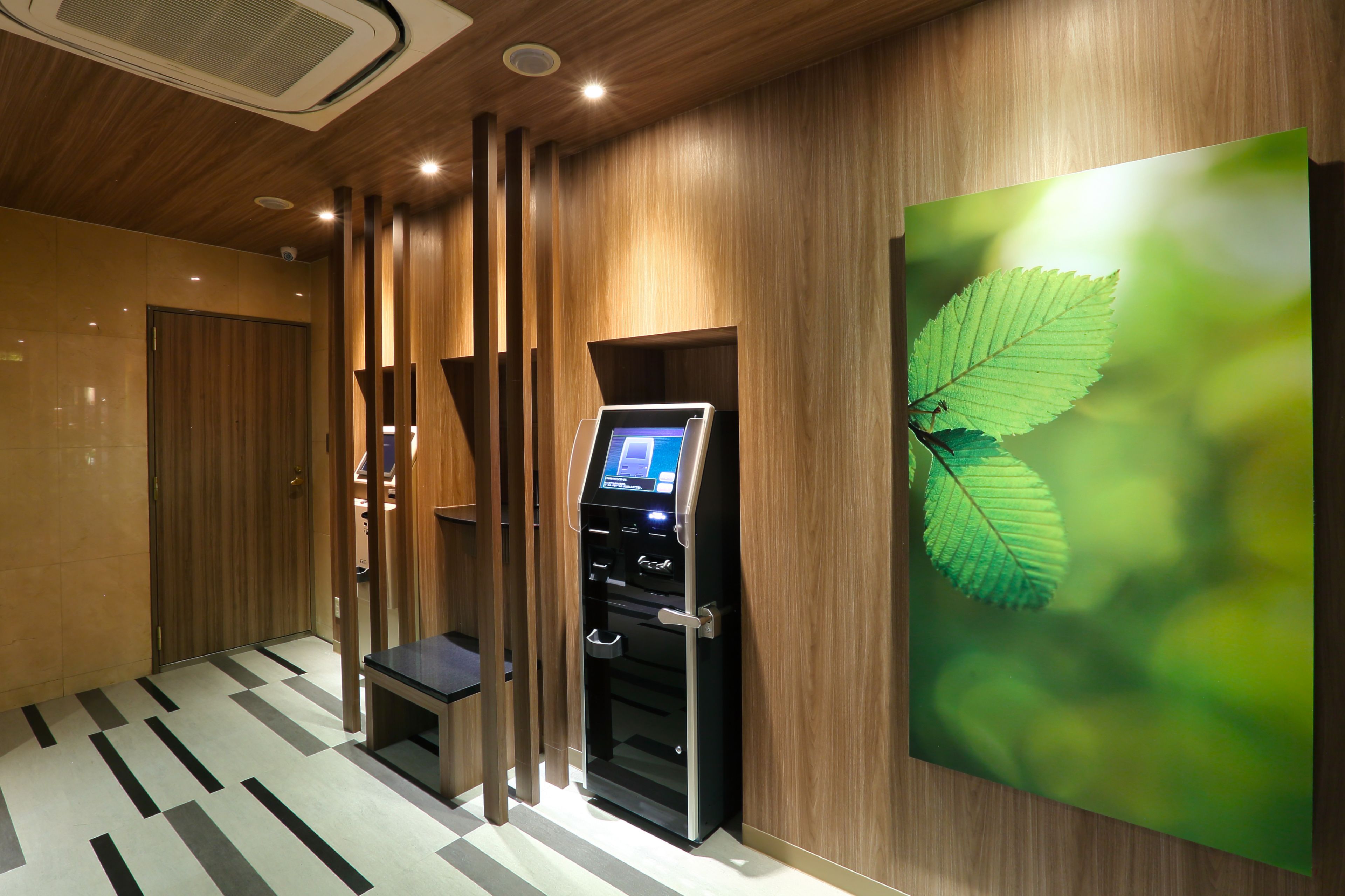 Un moderno vestíbulo de hotel con un quiosco digital, paneles de madera y una gran obra de arte con forma de hoja en la pared.