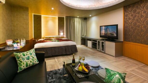 Ein Hotelzimmer mit einem Bett, einem Fernseher, einem Schreibtisch mit Computer und einem Couchtisch mit Obstschale.
