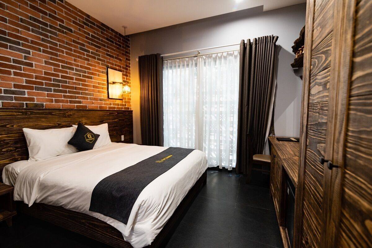Habitación de hotel con pared de ladrillo, cama con ropa de cama blanca, un plaid negro y cabecera de madera.