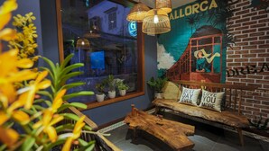 A cozy seating area with a wooden bench and cushions, a window with potted plants, and a mural on the wall. - The G.Hotel Hue - Hostel (Hue)