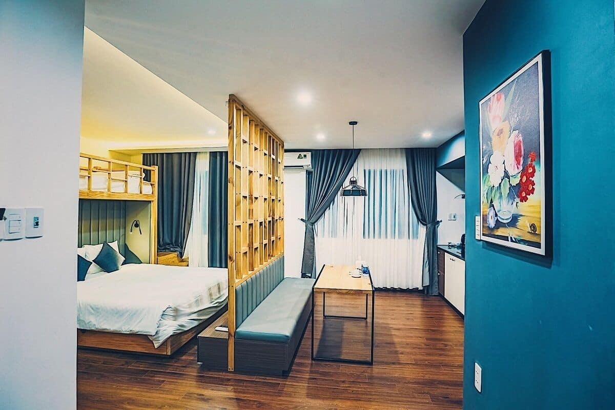 Habitación de hotel pequeña con una litera, un escritorio, una banca y un cuadro en la pared.