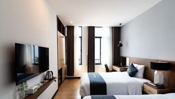 Habitación de hotel con dos camas, televisión, escritorio y ventana con cortinas.
