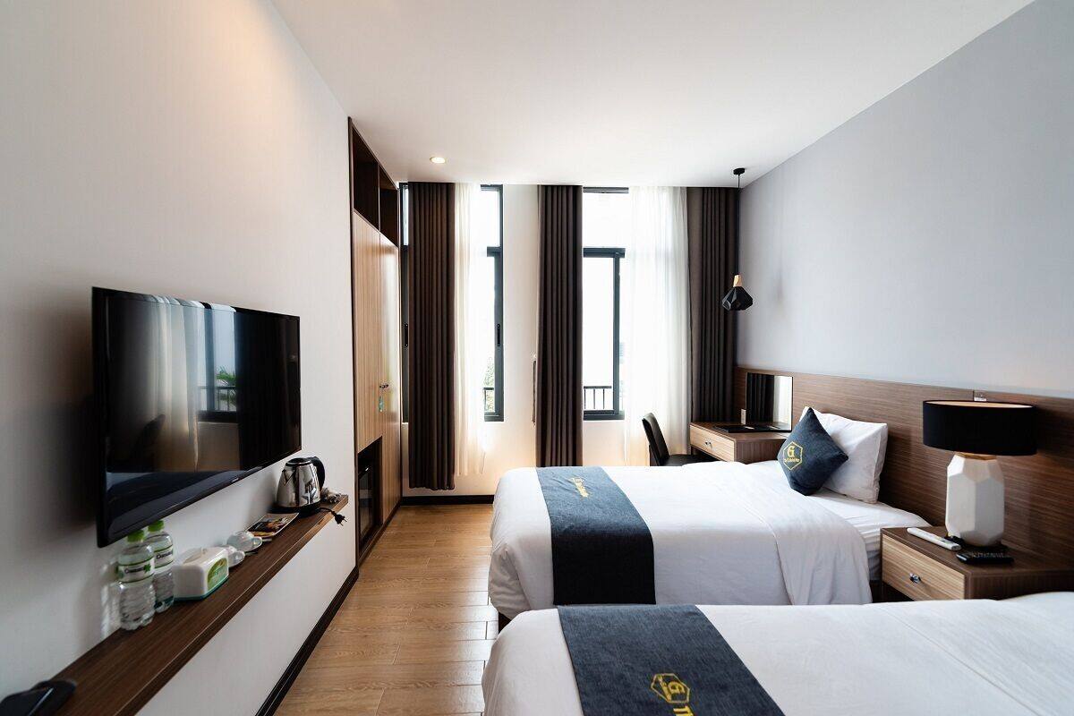 Habitación de hotel con dos camas, televisión, escritorio y ventana con cortinas.