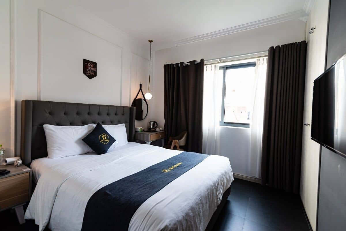 Habitación de hotel con una cama grande, un televisor de pantalla plana, un escritorio con lámpara y una ventana con cortinas.